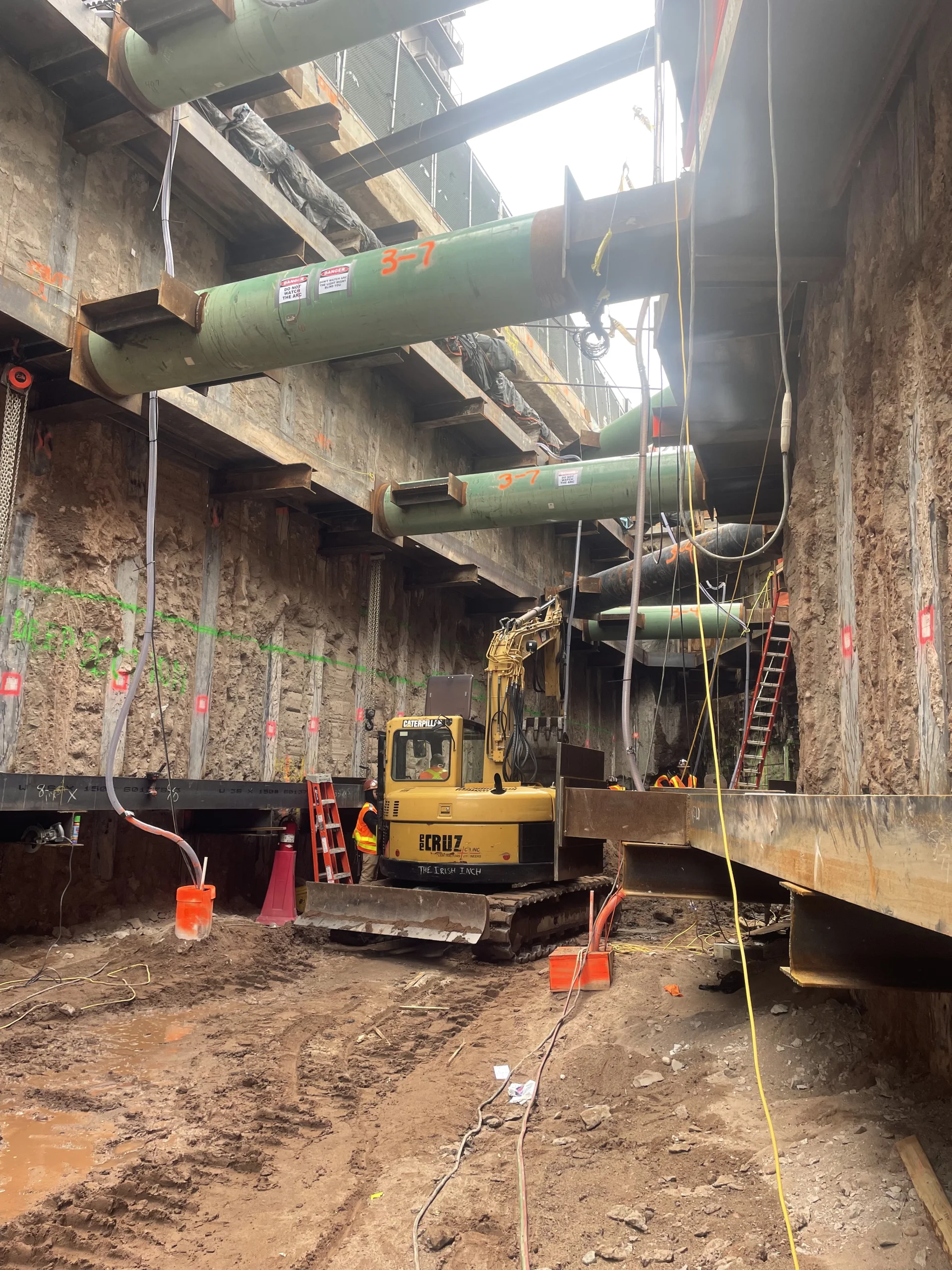 muddy construction site with large vehicles and green pipes